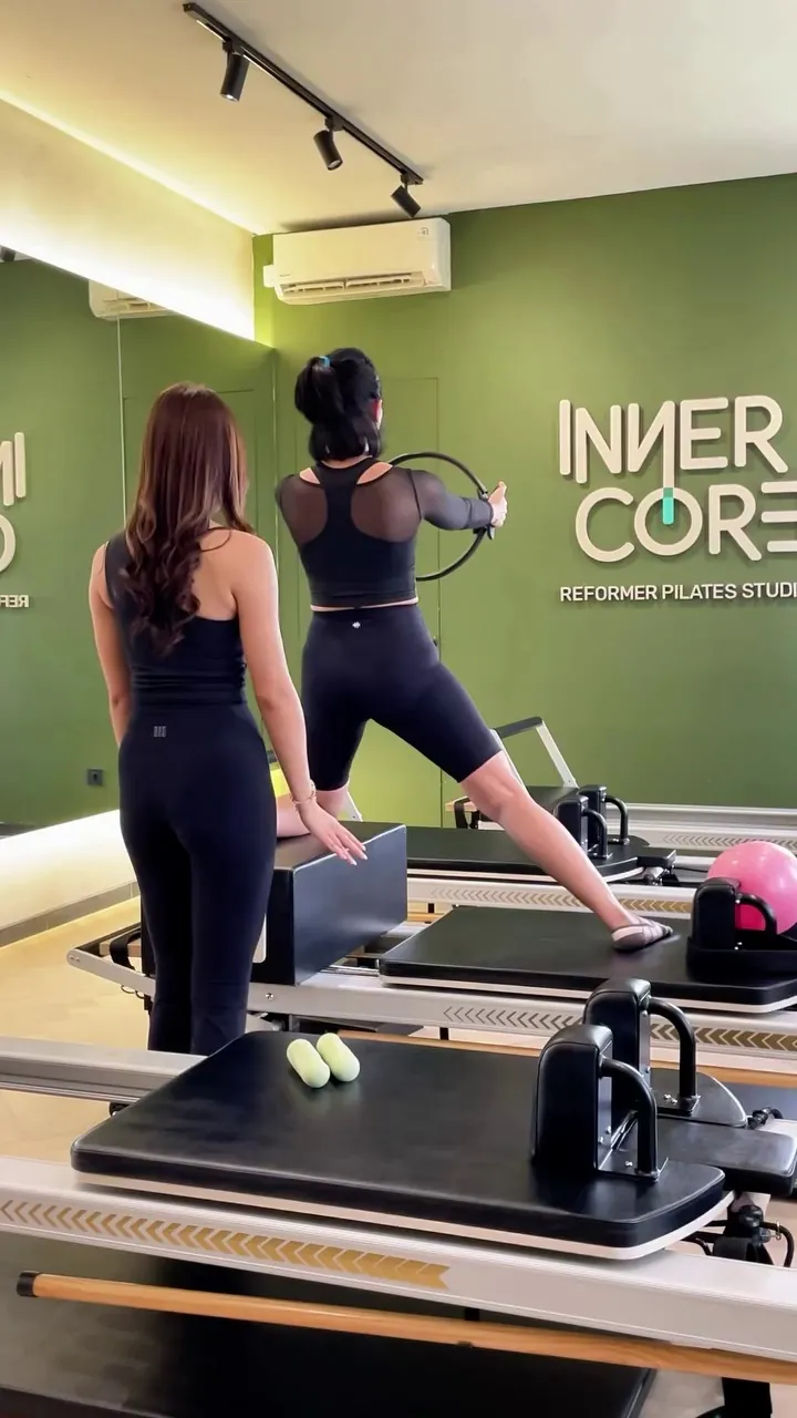 A coach guiding a client through a lunge on the reformer